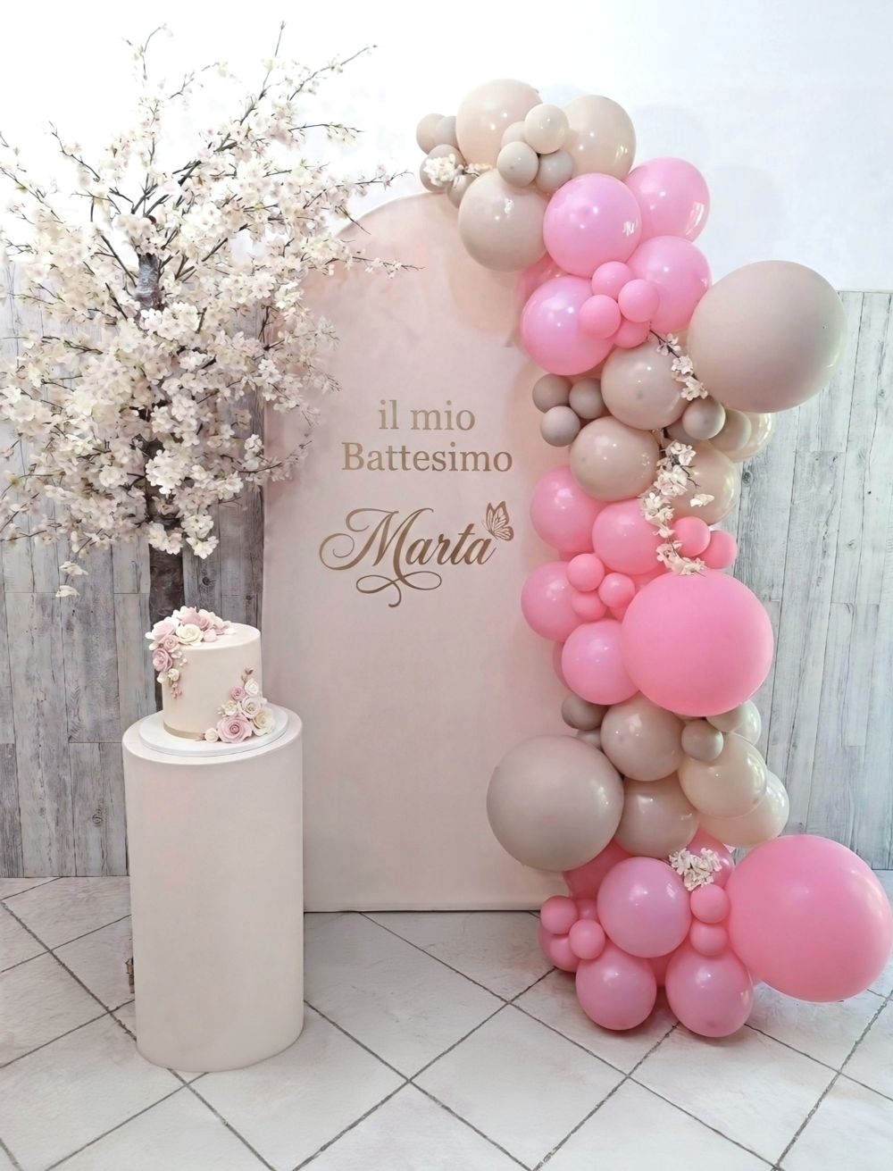 Allestimento Battesimo Marta Roma: scenografia rosa con arco di palloncini organici nei colori rosa e nude, albero di ciliegio artistico dipinto a mano e torta scenografica a tema.