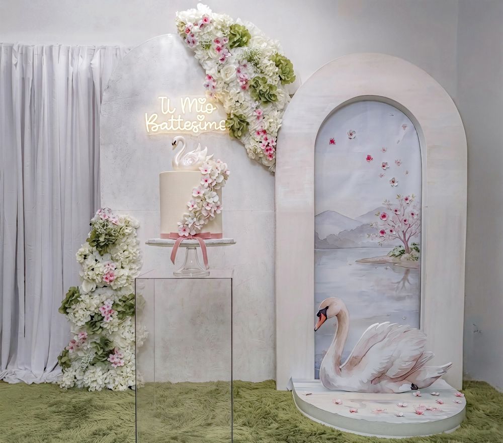 Allestimento battesimo tema cigno a Roma curato da Alessia Vincenti: fondale ad arco moderno, scultura di cigno dipinta a mano, composizione floreale artigianale e torta scenografica. Evento elegante ed esclusivo.