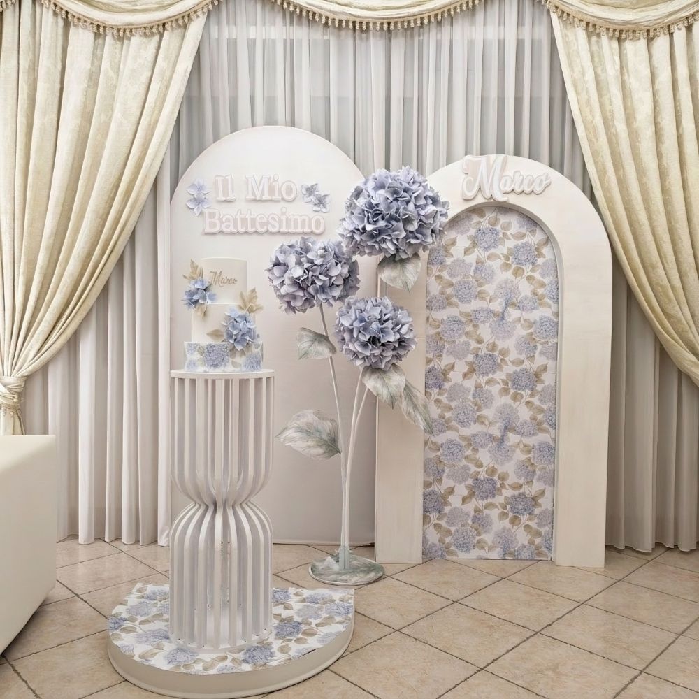 Allestimento scenografico elegante di Battesimo con fiori giganti di ortensia realizzati a mano, con decorazioni di carta decorativa di ortensie. Pedana piedistallo a listelli, torta scenografica a tema e scritta in rilievo il mio battesimo nei colori beige. Allestimento Battesimo realizzato a Roma da Alessia Vincenti