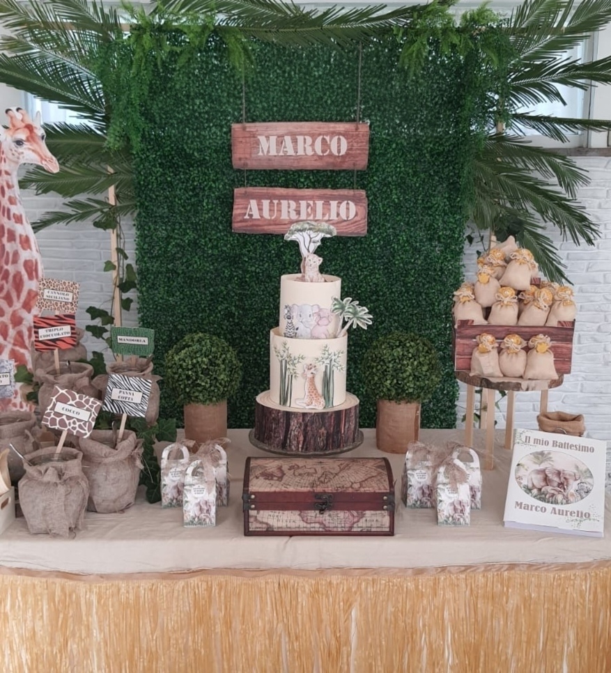 Allestimento Battesimo Tema Giungla con sagoma giraffa, parete verde di bosso con foglie di palma ed edera, nome su legno, scatoline personalizzate, confettata con segna gusti a tema, bomboniere e libro con grafica coordinata. Realizzato a Roma da Alessia Vincenti