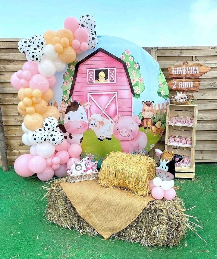 Allestimento tema fattoria realizzato a Roma da Alessia Vincenti con balla di fieno, semiarco di palloncini bianchi rosa gialli e motivo mucca, mobiletto per regalini fine festa realizzato con cassette di legno