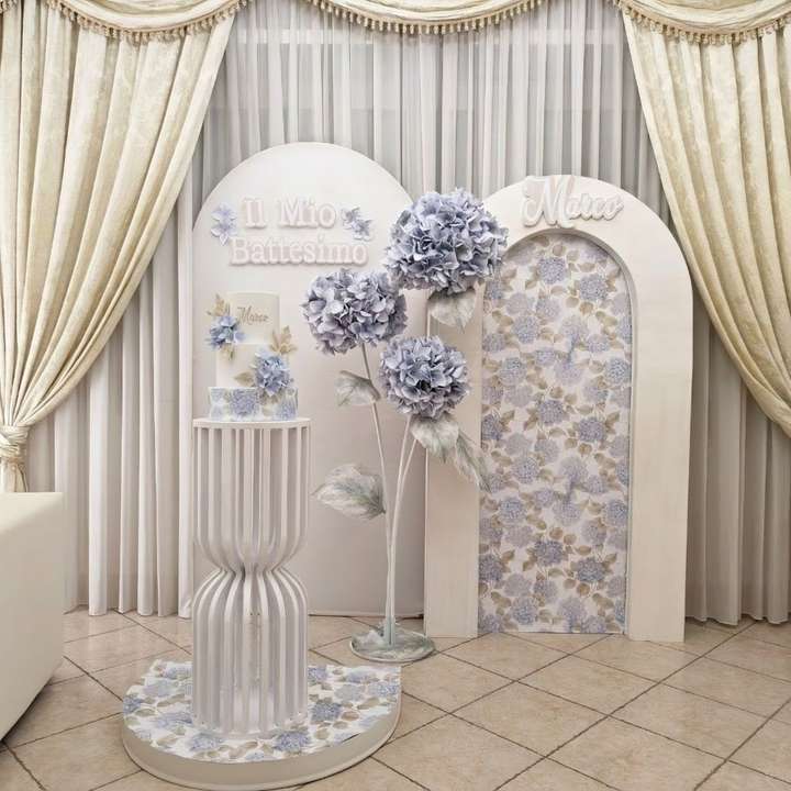 Allestimento tema battesimo con pedana e struttura decorate con carta di ortensia, torta scenografica e ortensia gigante. colori celeste polvere e verde polvere. carda decorativa, allestimento, fiore gigante, torta realizzati da Alessia Vincenti Roma